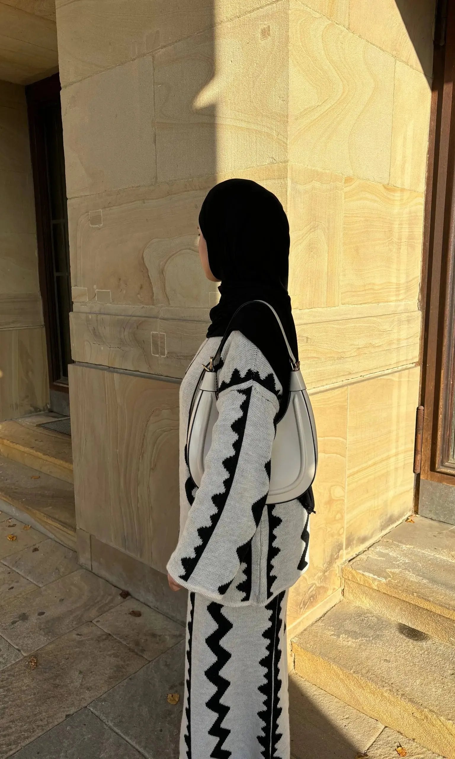 Ein grauer Strick-Zweiteiler mit Rock und schwarzem Zickzackmuster zeigt Modest Fashion mit weiten Ärmeln, Seitenansicht.