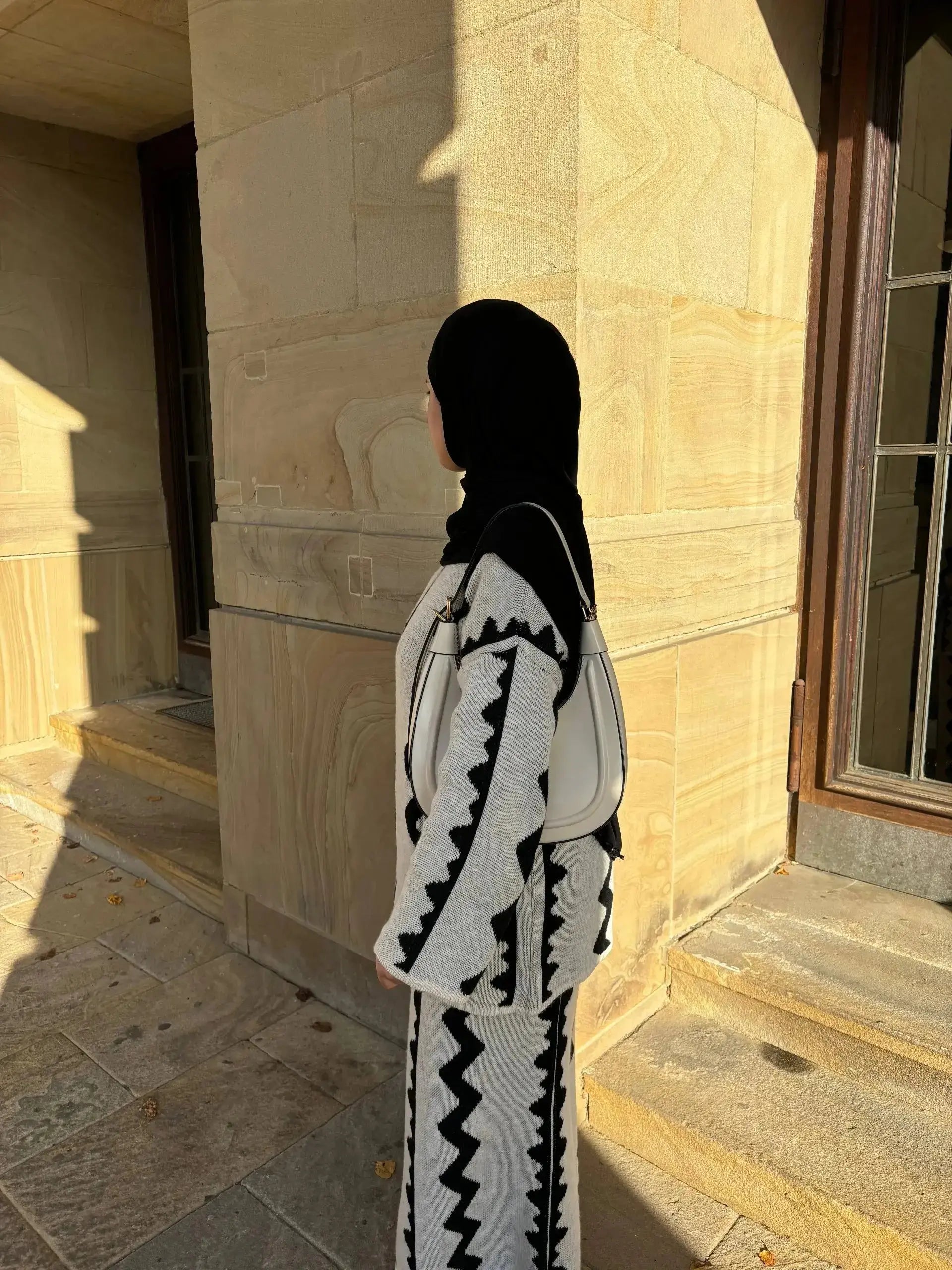 Ein grauer Strick-Zweiteiler mit Rock und schwarzem Zickzackmuster zeigt Modest Fashion mit weiten Ärmeln, Seitenansicht.