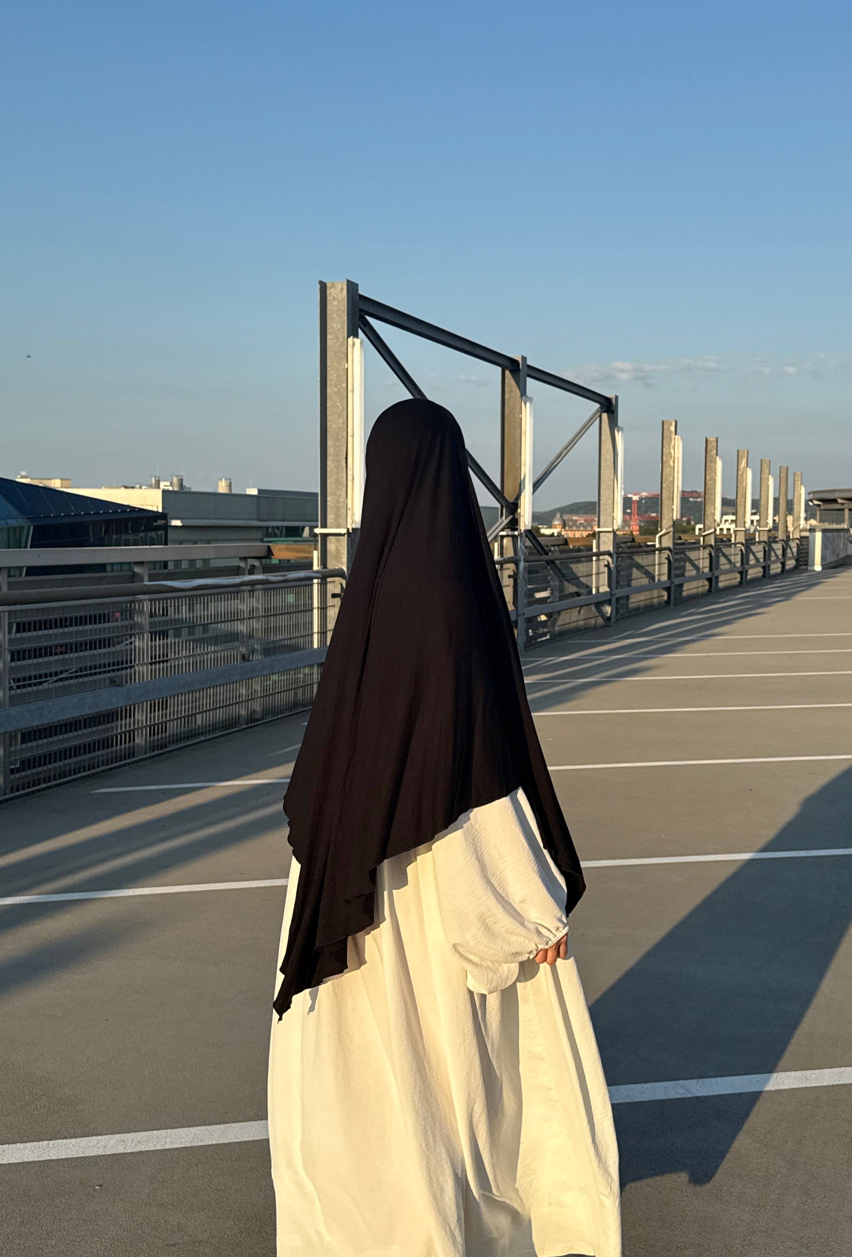 Jersey Khimar aus Viskose‑Elastan in Schwarz, Rückansicht einer Trägerin auf Parkdeck.