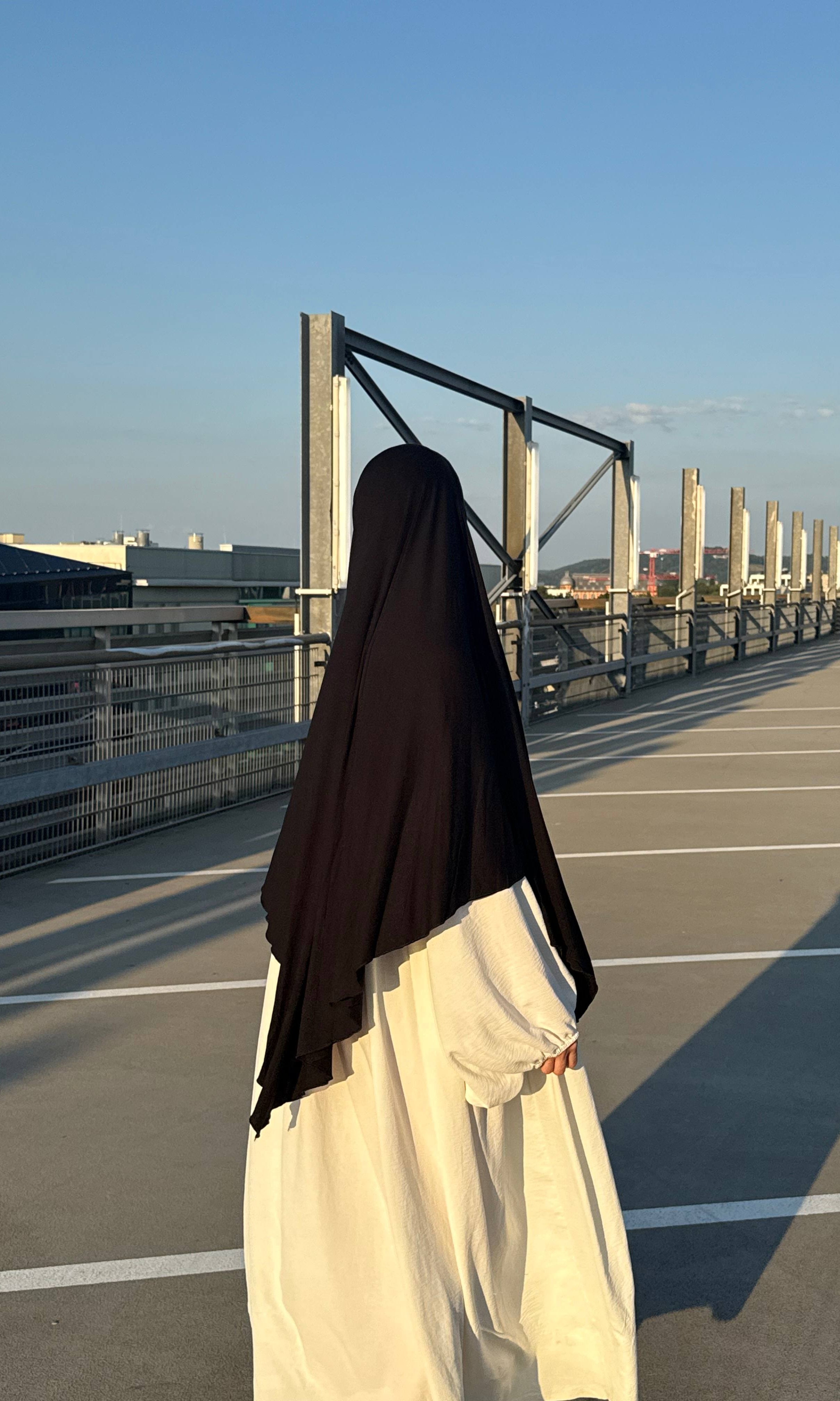 Jersey Khimar aus Viskose‑Elastan in Schwarz, Rückansicht einer Trägerin auf Parkdeck.