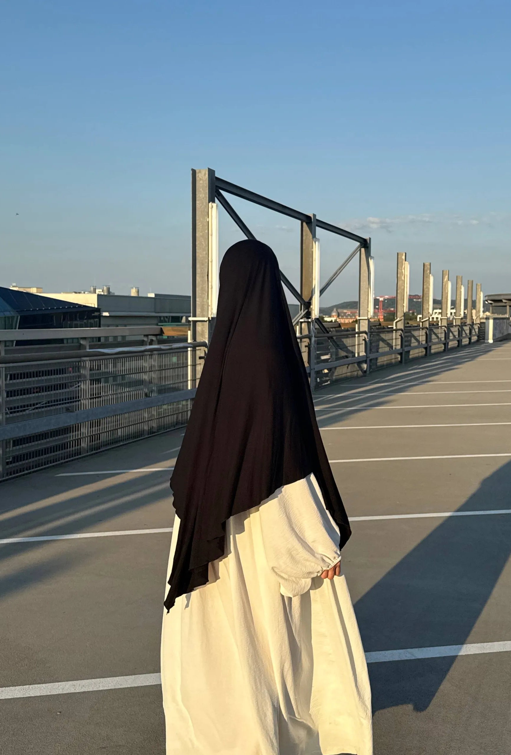 Jersey Khimar aus Viskose‑Elastan in Schwarz, Rückansicht einer Trägerin auf Parkdeck.