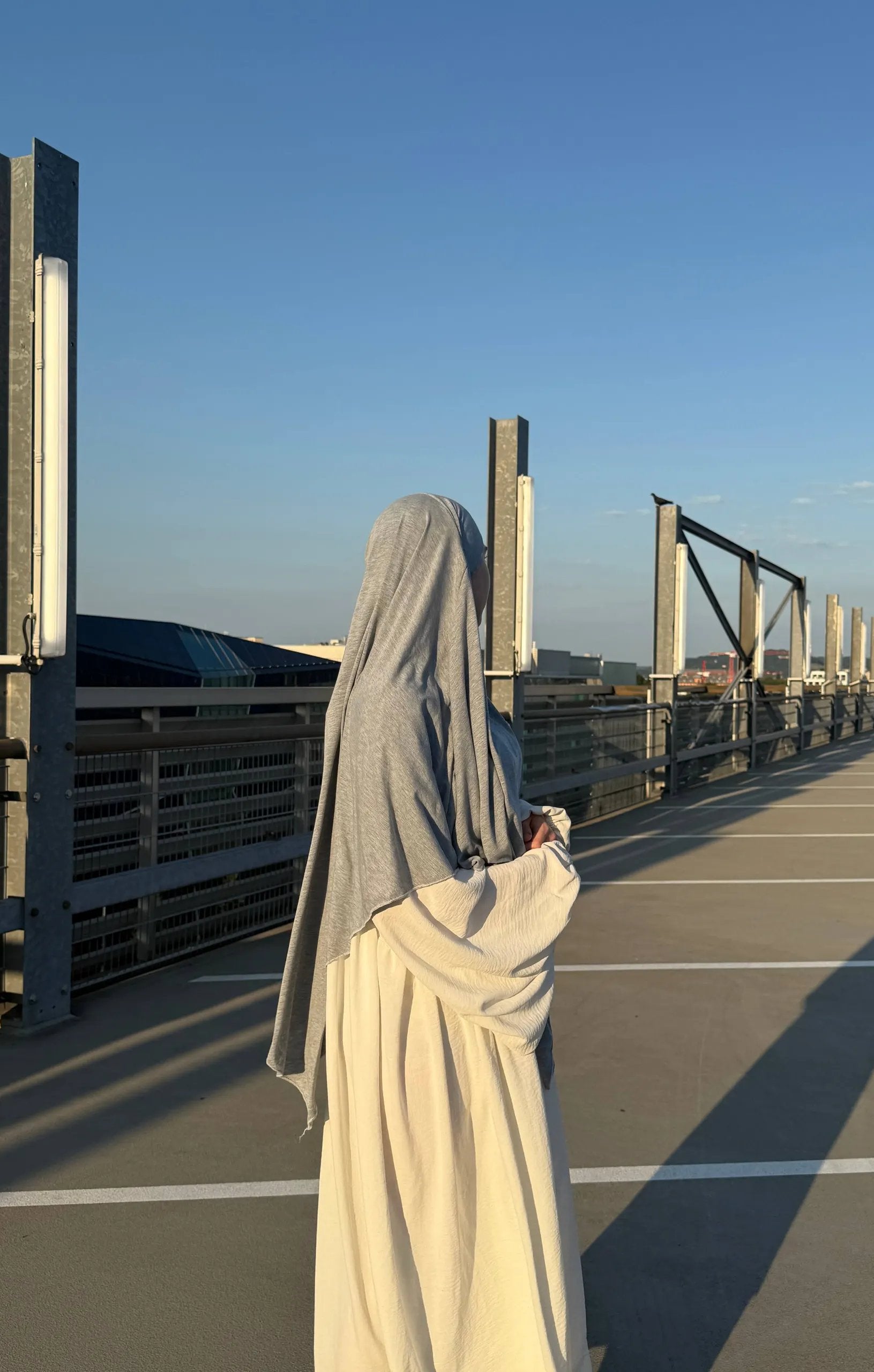 Eine Person trägt einen hellgrauen Jersey-Khimar aus Viskose-Elastan, seitliche Rückenansicht.