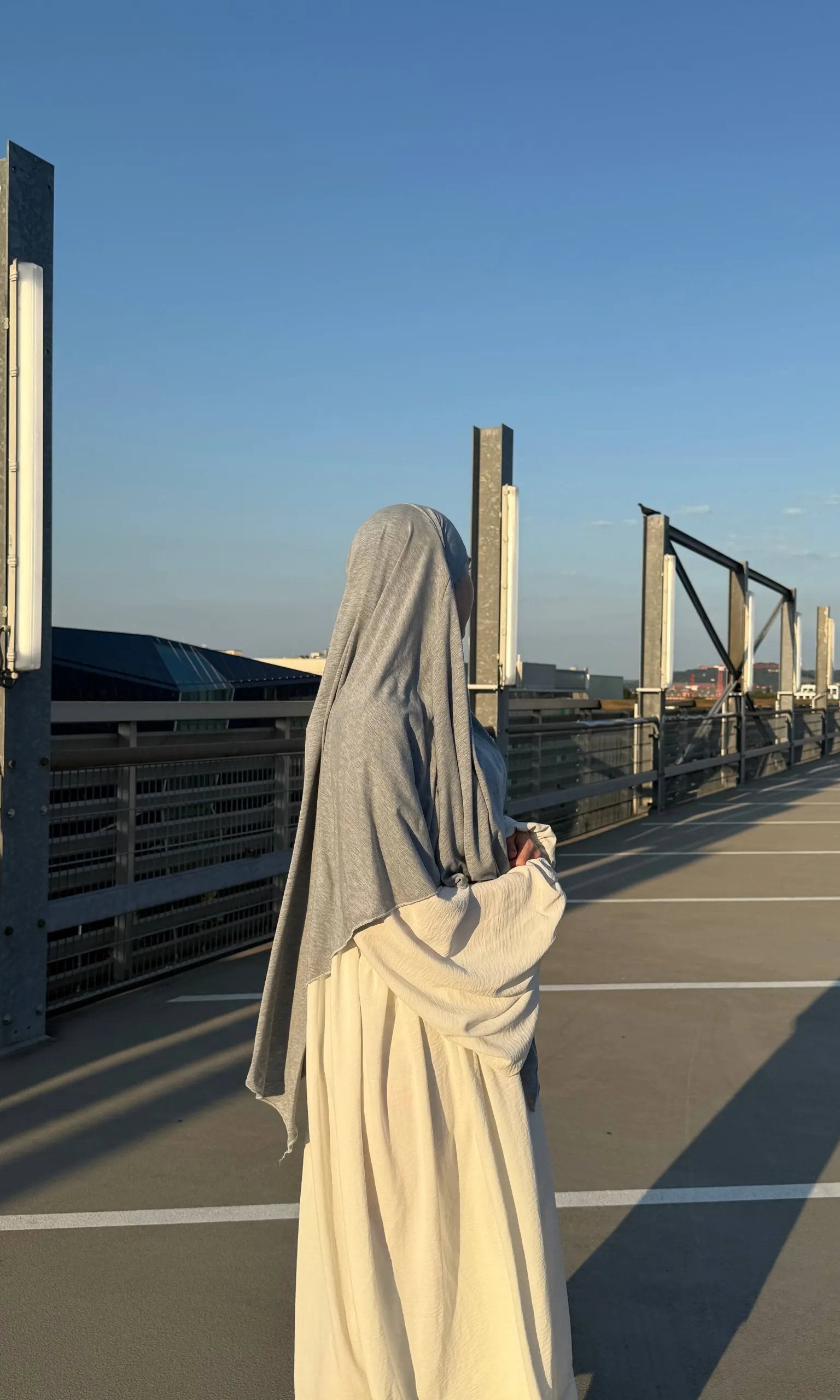 Eine Person trägt einen hellgrauen Jersey-Khimar aus Viskose-Elastan, seitliche Rückenansicht.