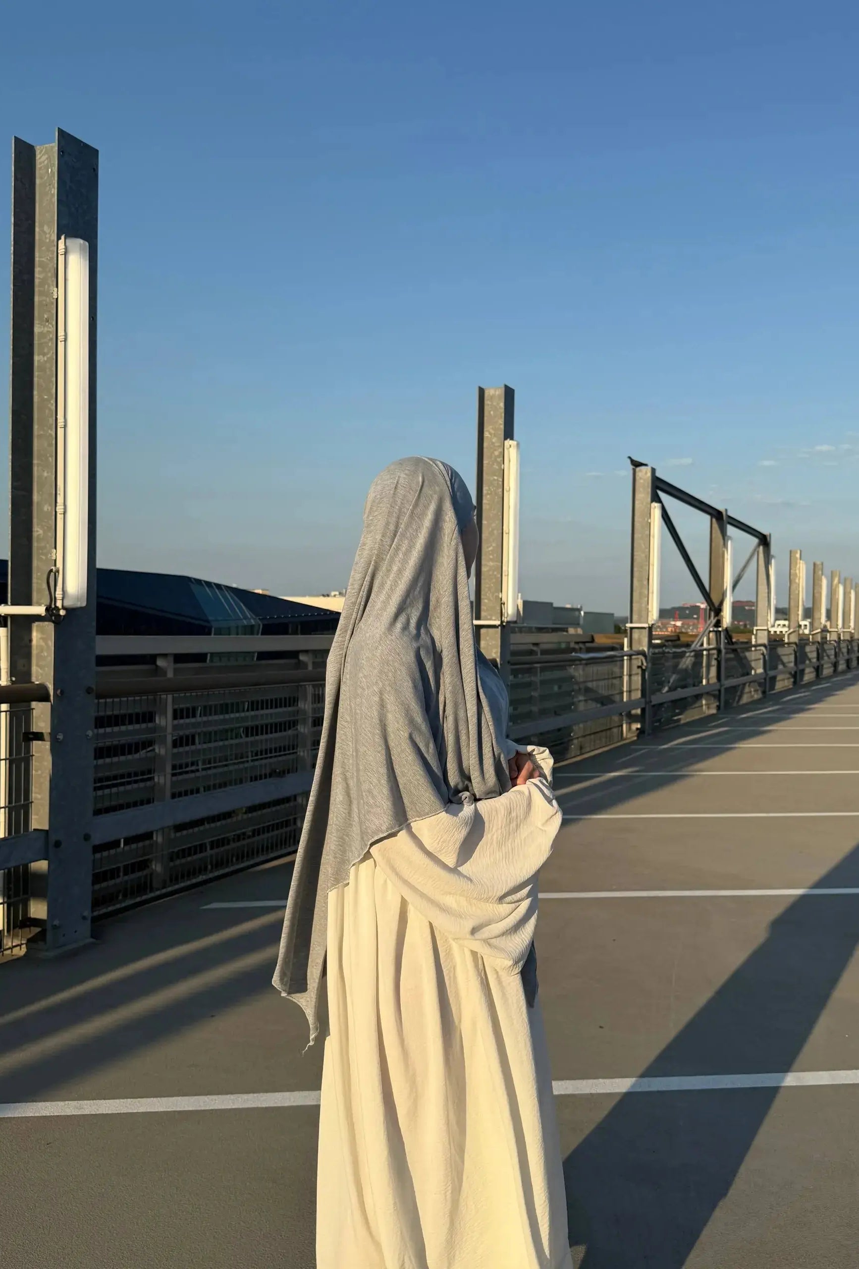 Eine Person trägt einen hellgrauen Jersey-Khimar aus Viskose-Elastan, seitliche Rückenansicht.