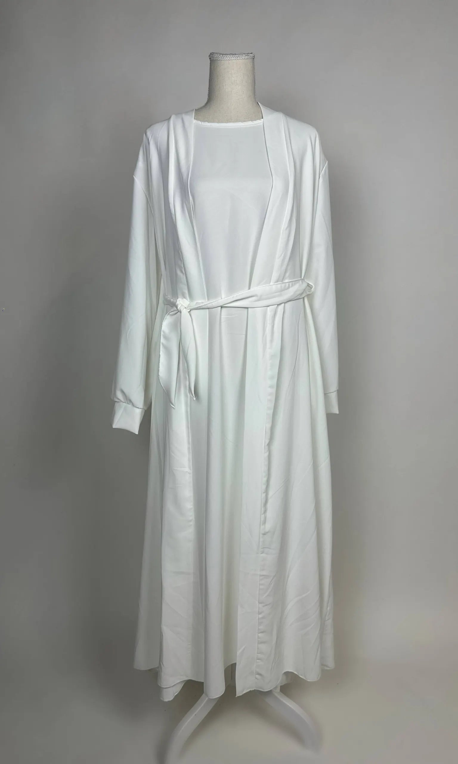 Eine weiße Open-Abaya im Dubai-Stil aus Medina-Seide mit Unterkleid und Bindegürtel wird in Vorderansicht gezeigt.