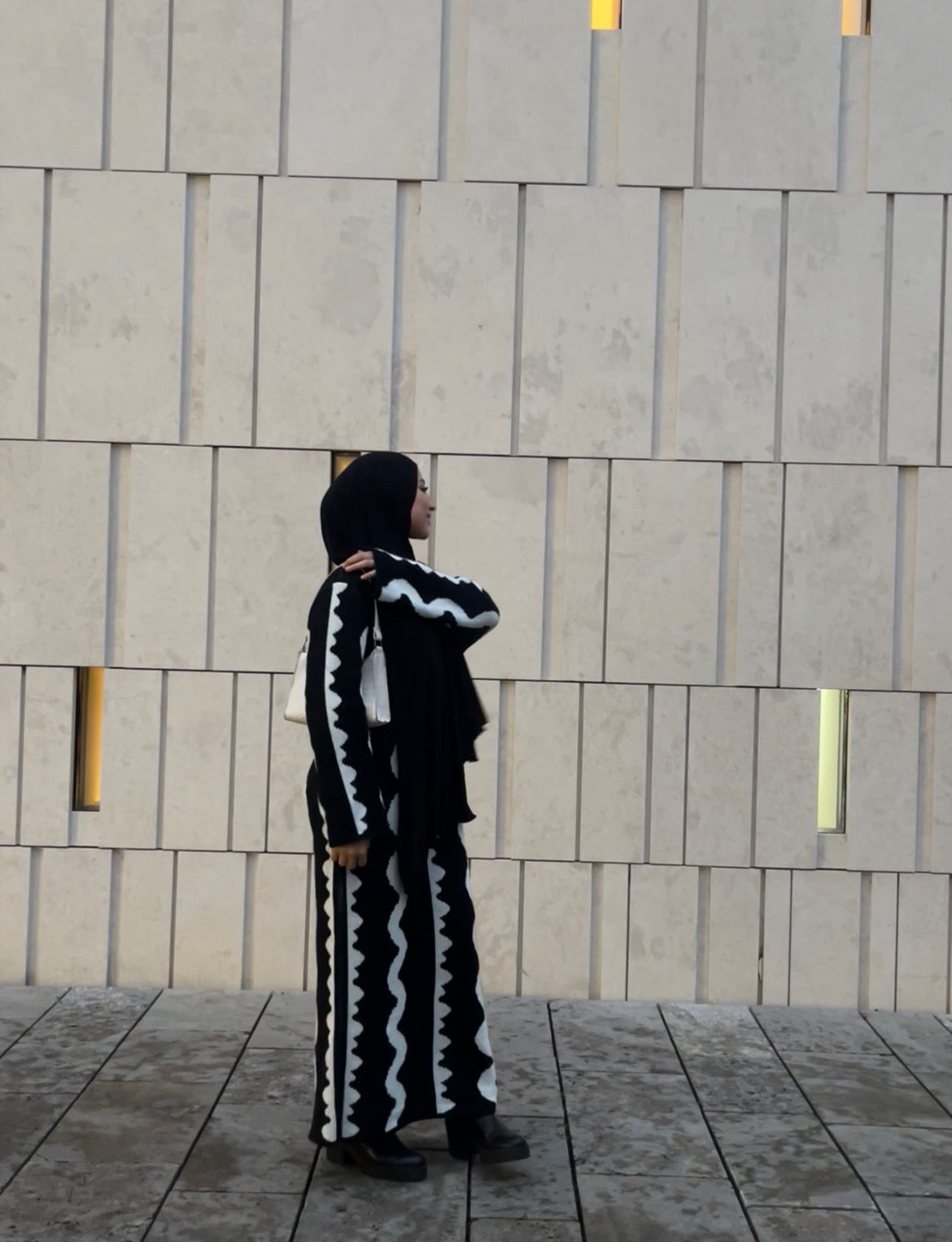 Schwarzes Maxi-Strickkleid mit weißen Zickzack-Streifen und langen Ärmeln, wärmendes Material, Seitenansicht.