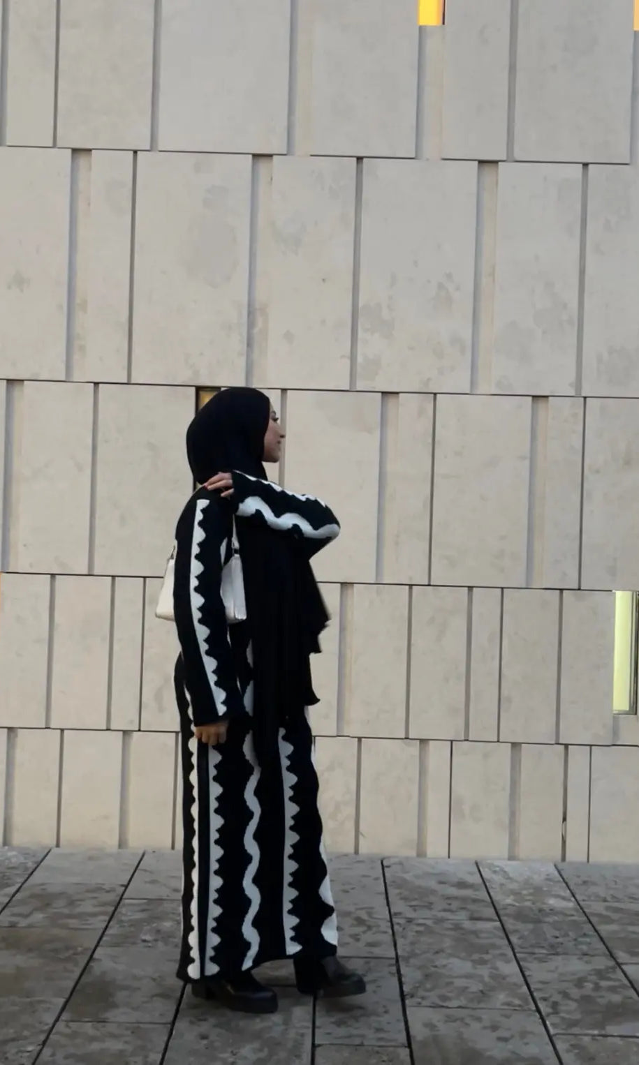 Schwarzes Maxi-Strickkleid mit weißen Zickzack-Streifen und langen Ärmeln, wärmendes Material, Seitenansicht.