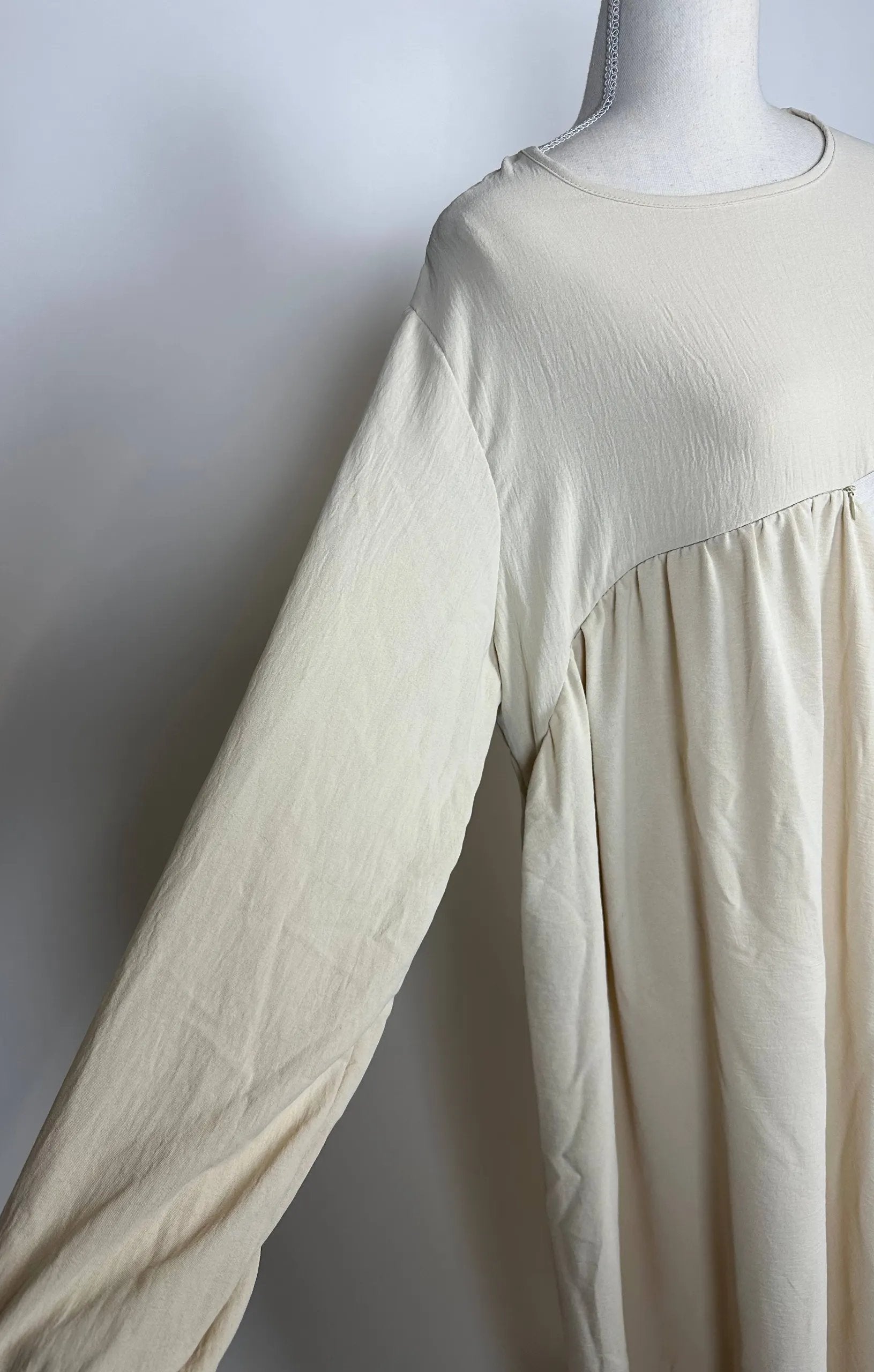 Cremefarbene Still-Abaya aus luftigem Jazzstoff mit verdeckter Stillöffnung, Detailansicht der Vorderseite.