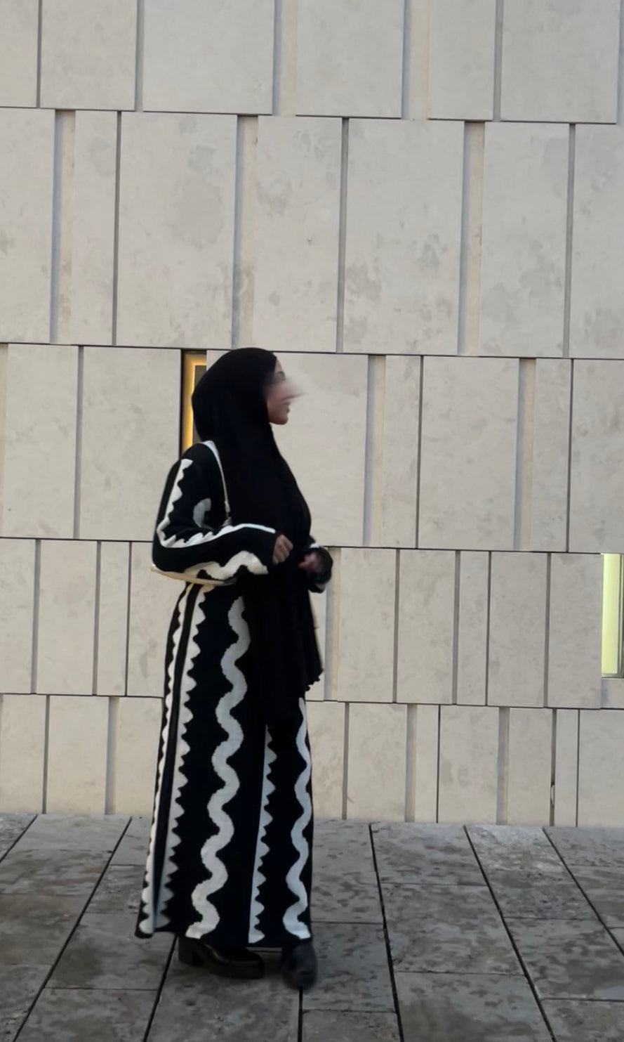 Zu sehen ist ein schwarzes Maxi Strickkleid mit weißen Wellenstreifen und langen Ärmeln, Seitenansicht.