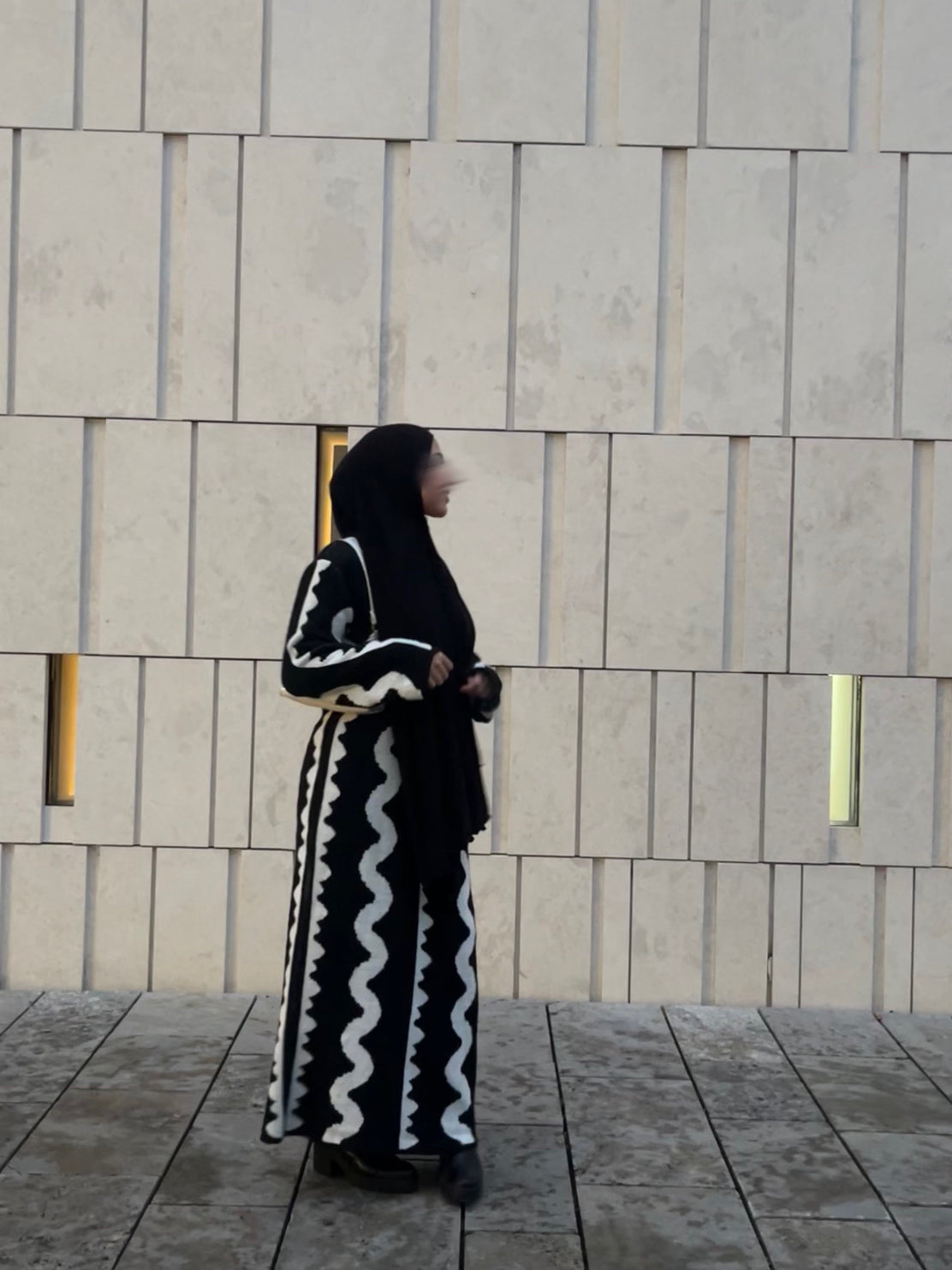 Zu sehen ist ein schwarzes Maxi Strickkleid mit weißen Wellenstreifen und langen Ärmeln, Seitenansicht.