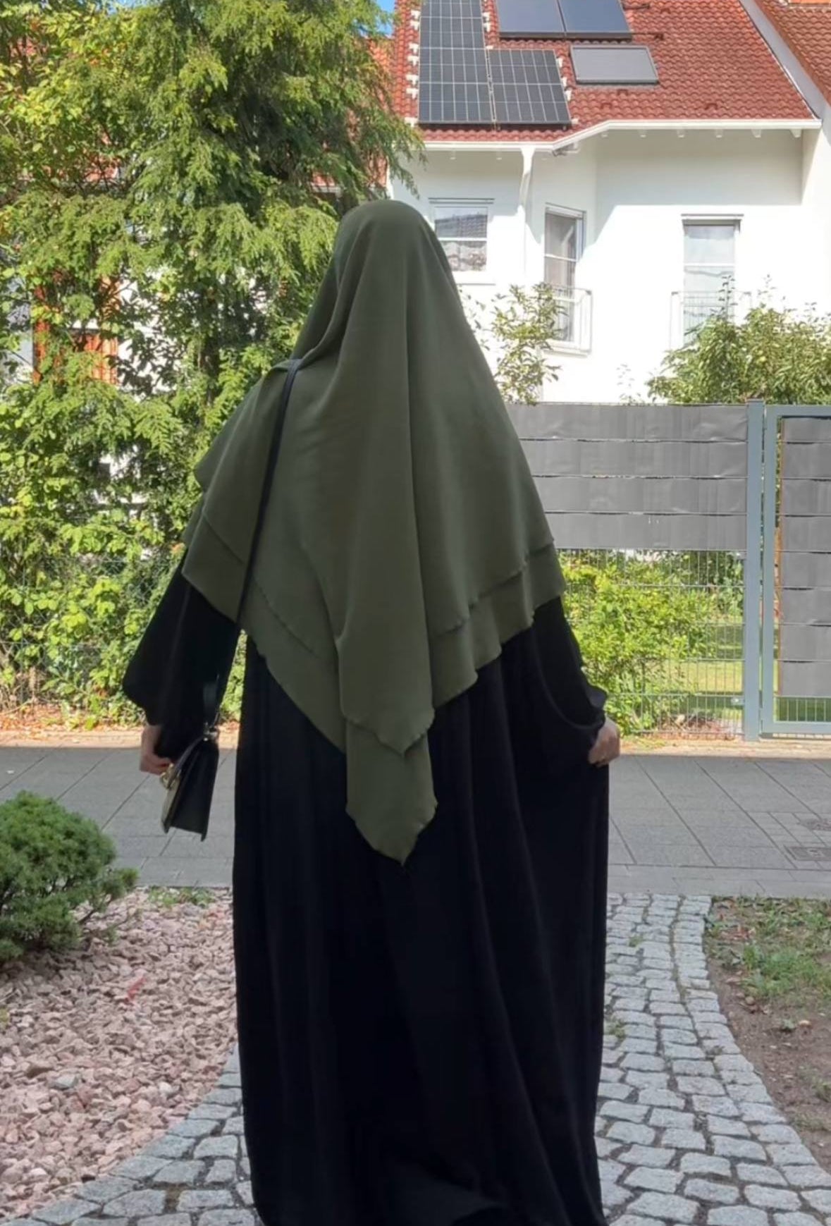 Ein olivgrüner Khimar aus Jazz liegt zweilagig über einer schwarzen Abaya, in Rückansicht.