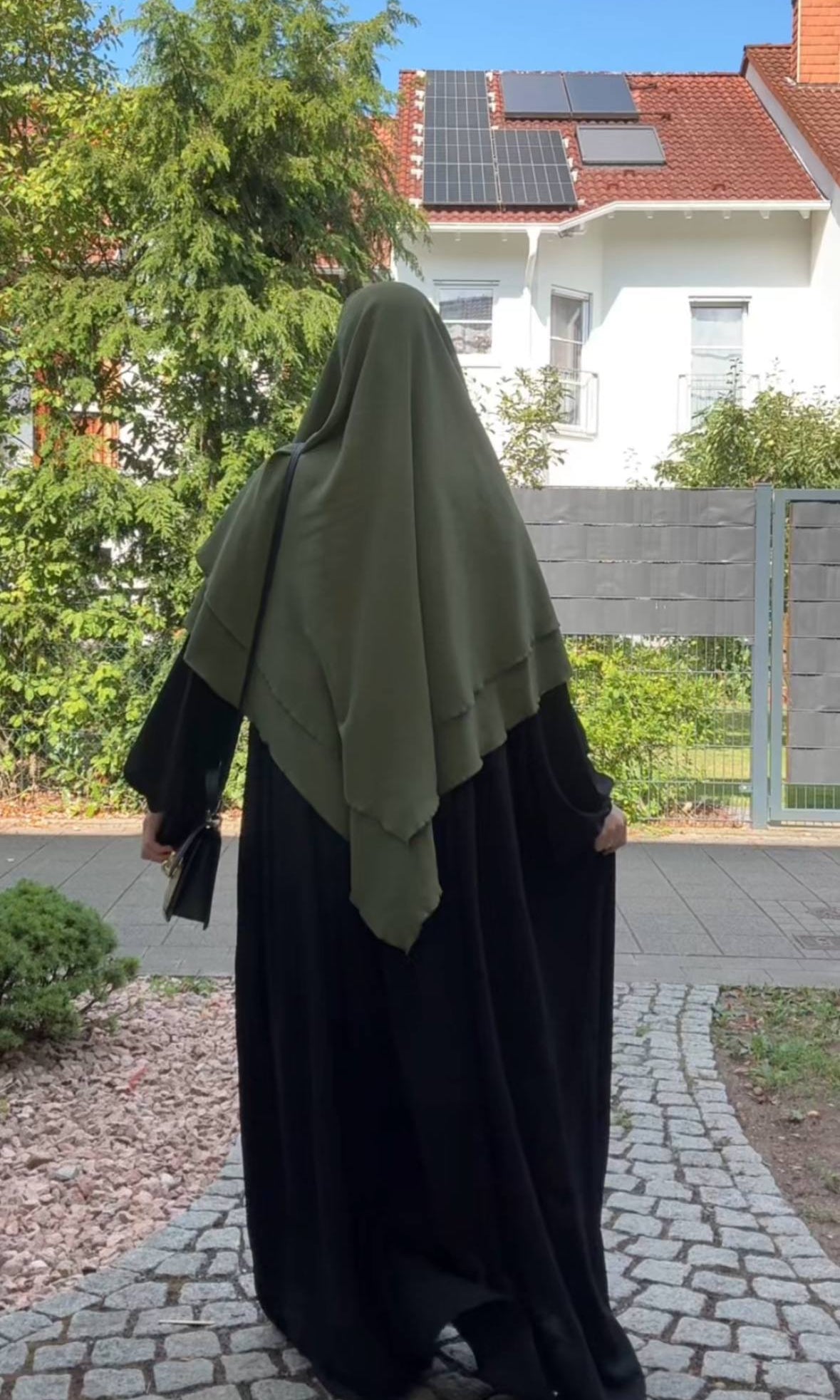Ein olivgrüner Khimar aus Jazz liegt zweilagig über einer schwarzen Abaya, in Rückansicht.