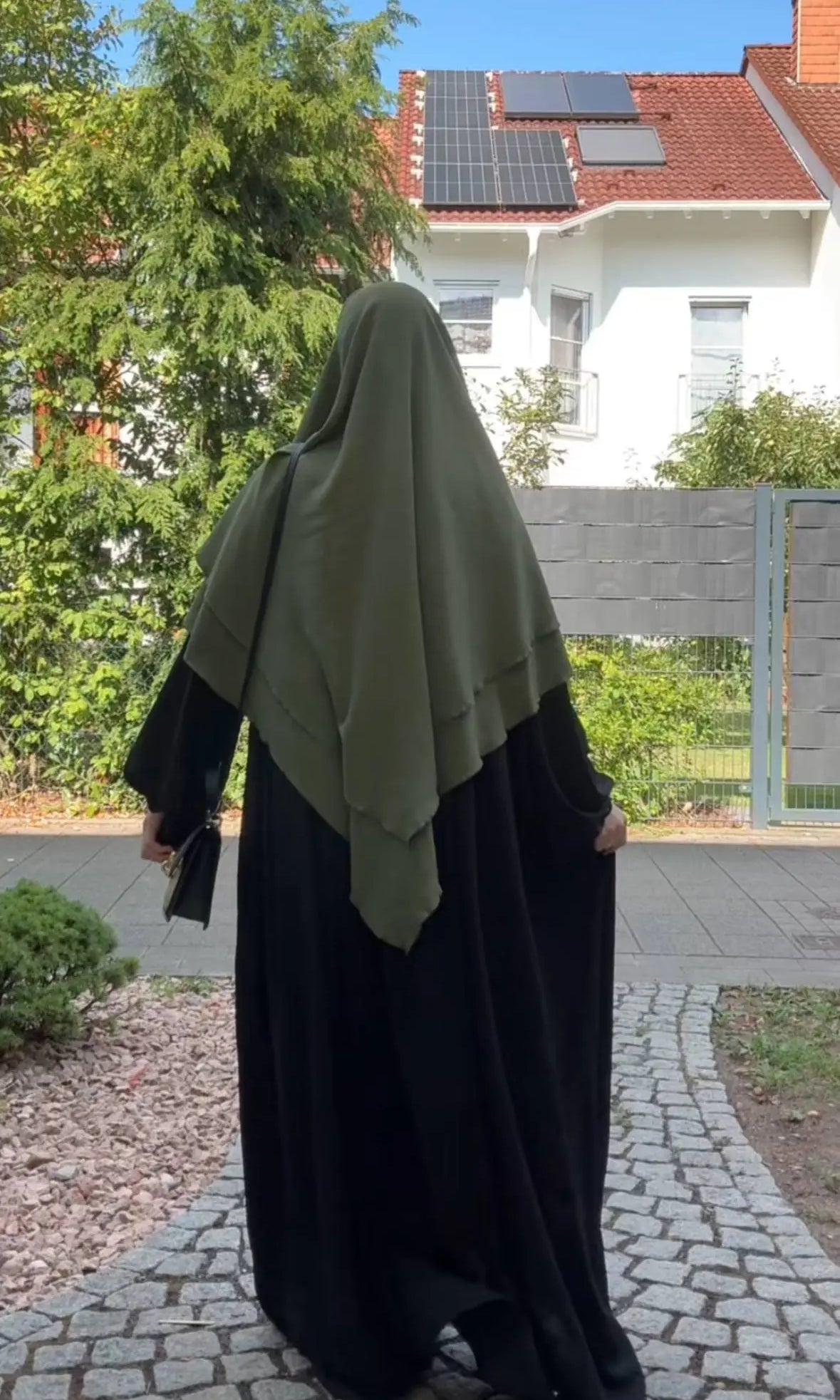 Ein olivgrüner Khimar aus Jazz liegt zweilagig über einer schwarzen Abaya, in Rückansicht.