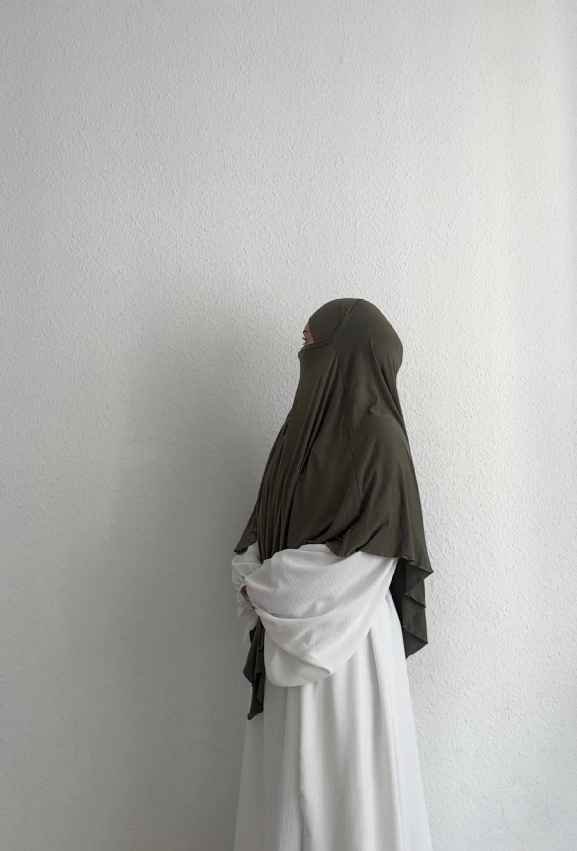 Eine Person trägt einen Jersey Khimar aus Viskose-Elastan in Oliv, seitliche Ganzkörperansicht.