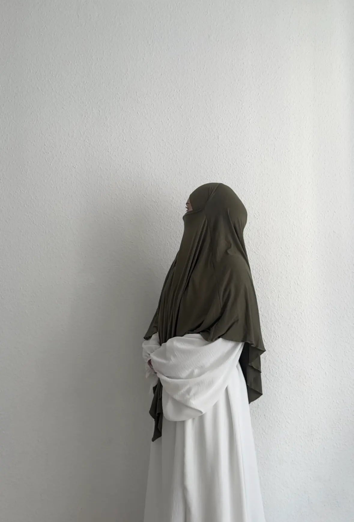 Eine Person trägt einen Jersey Khimar aus Viskose-Elastan in Oliv, seitliche Ganzkörperansicht.