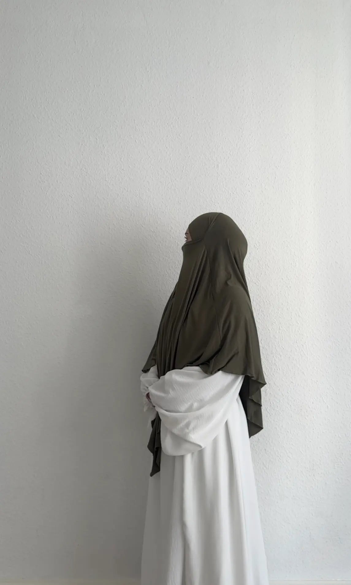 Eine Person trägt einen Jersey Khimar aus Viskose-Elastan in Oliv, seitliche Ganzkörperansicht.