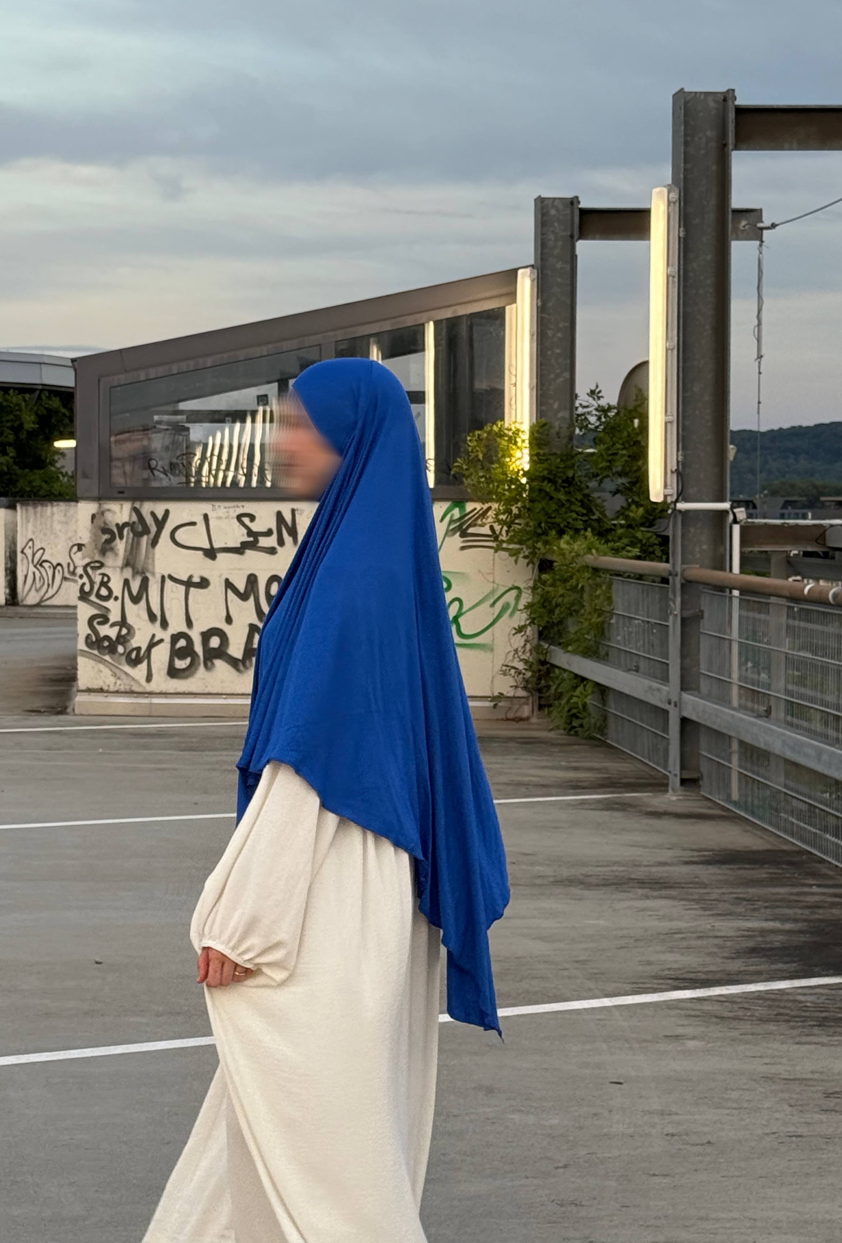 Ein Modell trägt einen blauen Jersey‑Khimar aus Viskose‑Elastan (95/5), Seitenansicht.