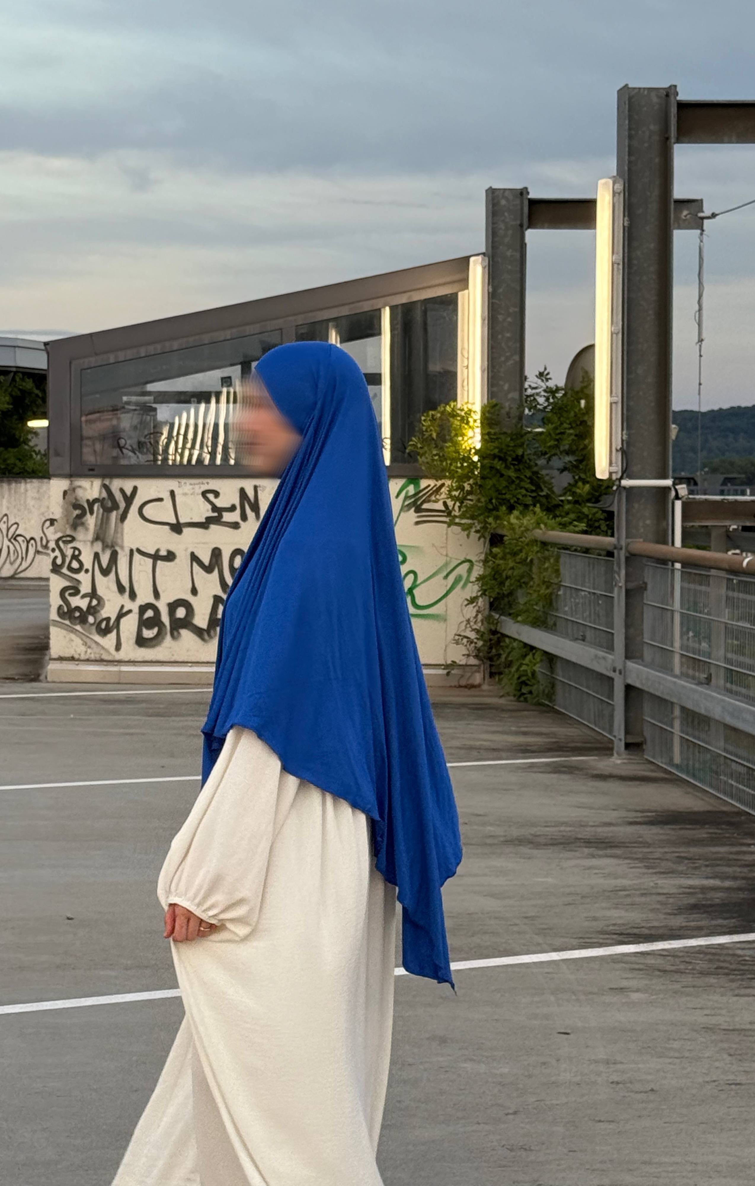 Ein Modell trägt einen blauen Jersey‑Khimar aus Viskose‑Elastan (95/5), Seitenansicht.