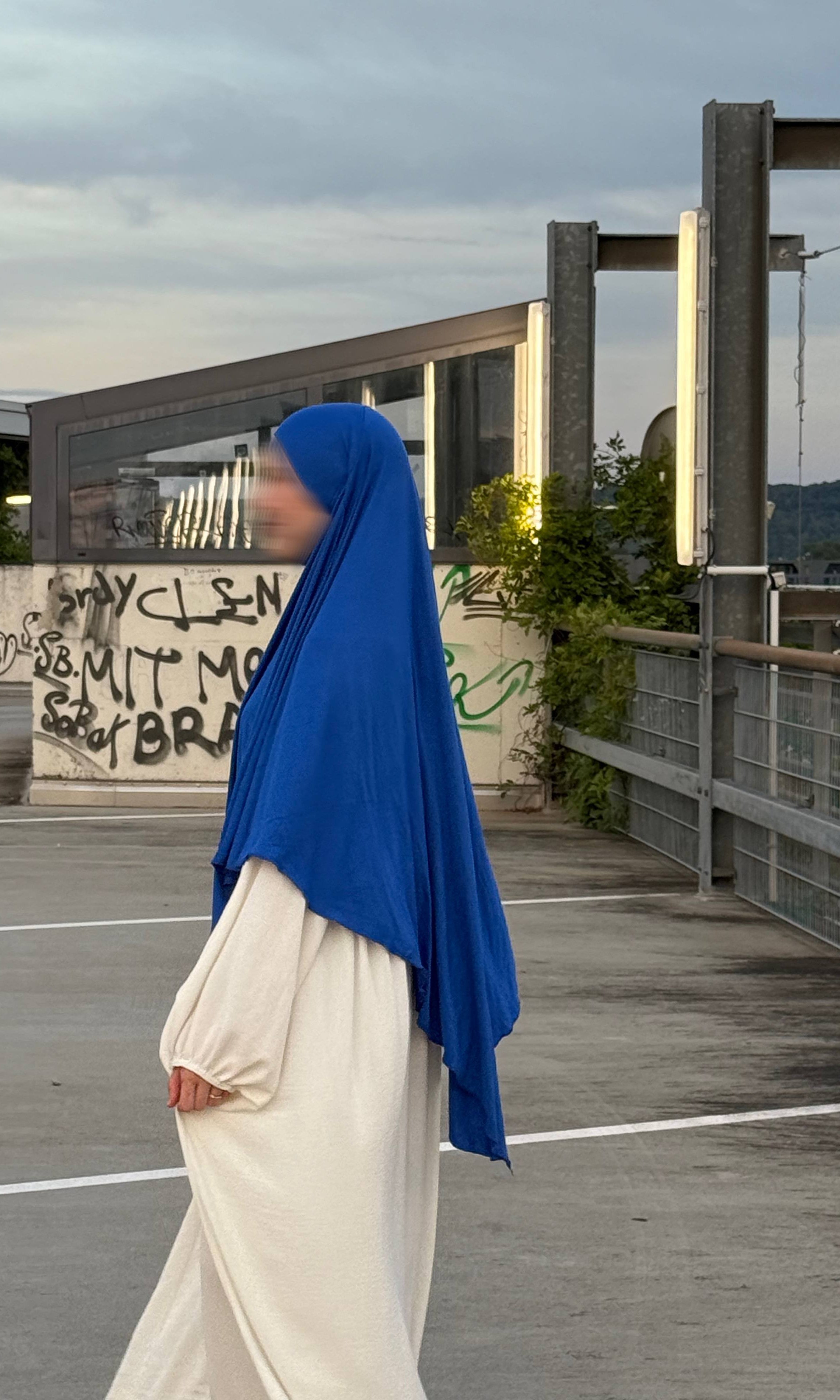 Ein Modell trägt einen blauen Jersey‑Khimar aus Viskose‑Elastan (95/5), Seitenansicht.