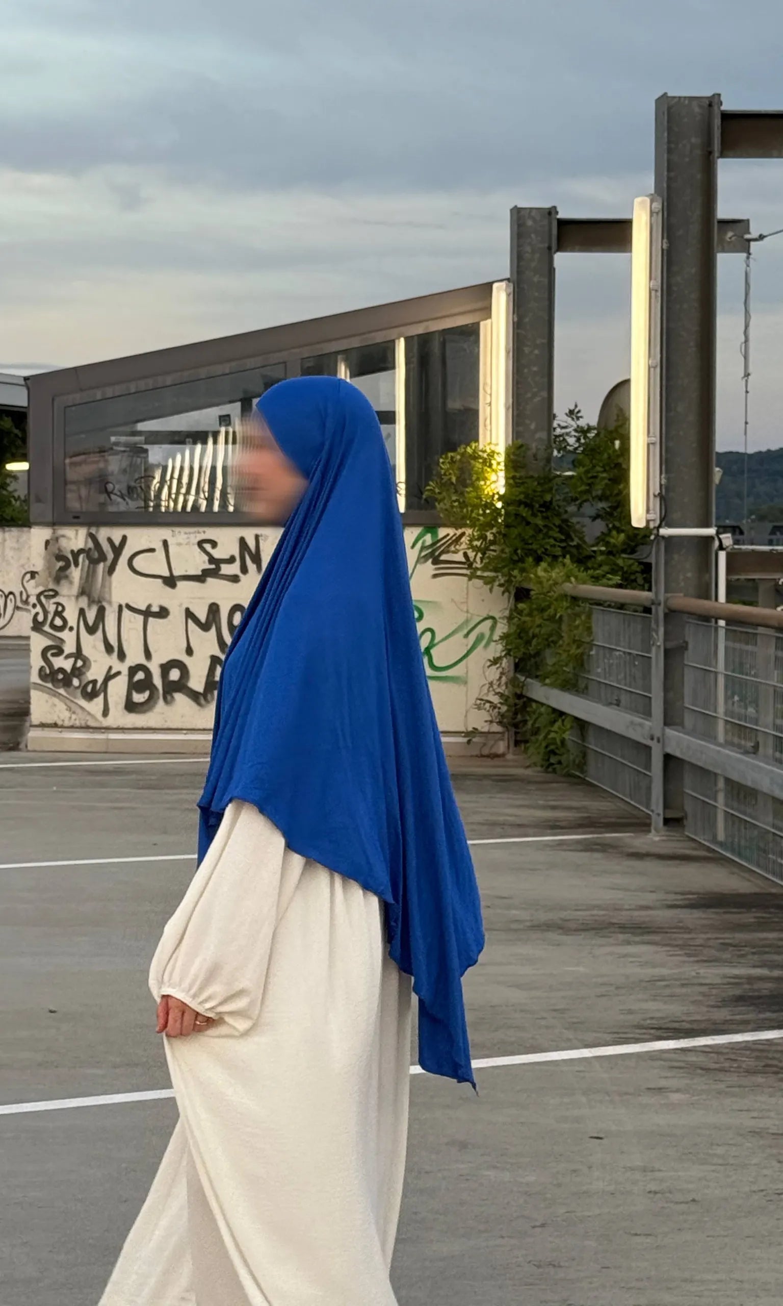 Ein Modell trägt einen blauen Jersey‑Khimar aus Viskose‑Elastan (95/5), Seitenansicht.