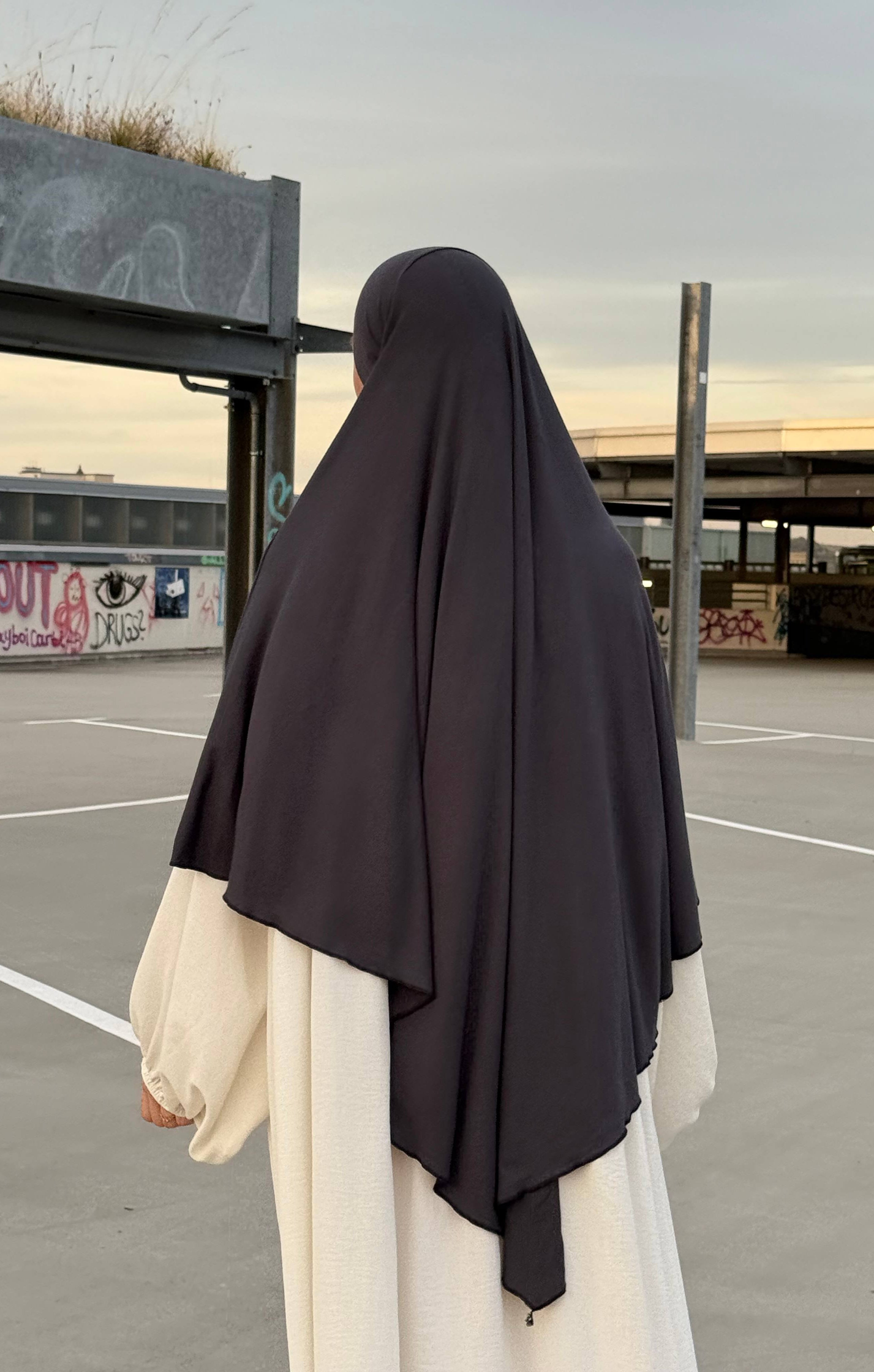 Eine Person trägt einen dunkelgrauen Jersey‑Khimar aus Viskose‑Elastan in Rückenansicht.