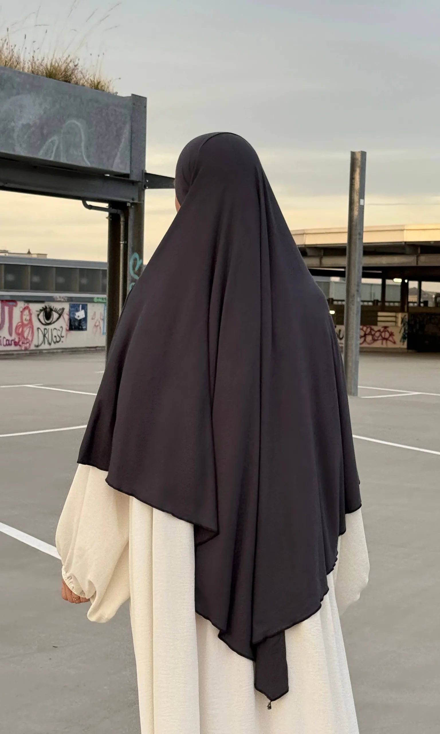 Eine Person trägt einen dunkelgrauen Jersey‑Khimar aus Viskose‑Elastan in Rückenansicht.