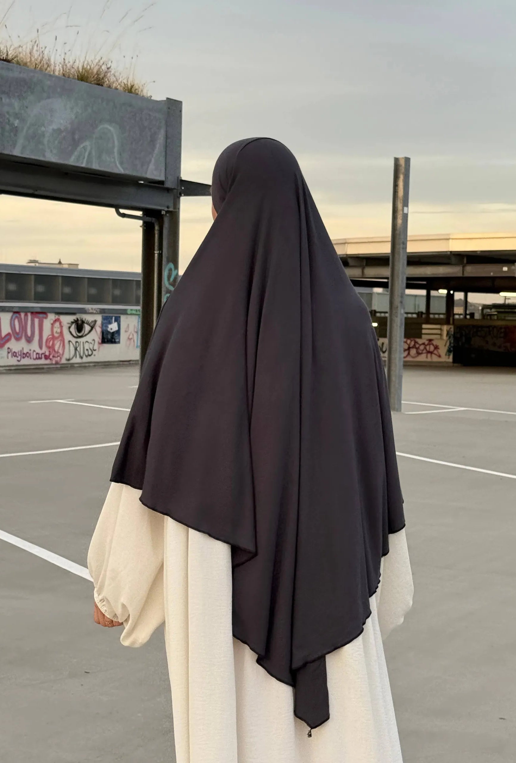 Eine Person trägt einen dunkelgrauen Jersey‑Khimar aus Viskose‑Elastan in Rückenansicht.