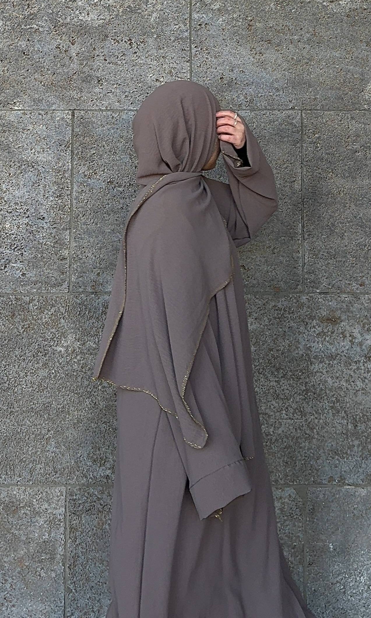 Taupefarbene Einteiler-Abaya aus fließendem Stoff mit integriertem Hijab und goldener Paspel, Seitenansicht.