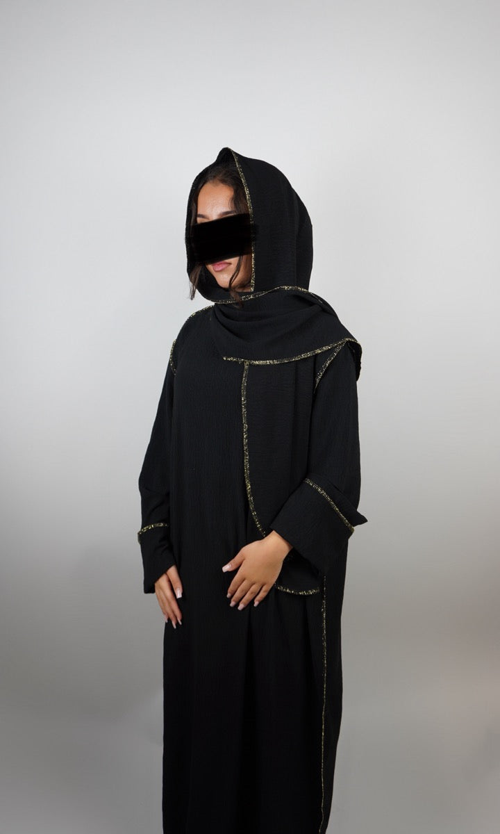 Schwarze Einteiler-Abaya aus strukturiertem Stoff mit integriertem Hijab und goldener Paspel, Dreiviertelansicht.