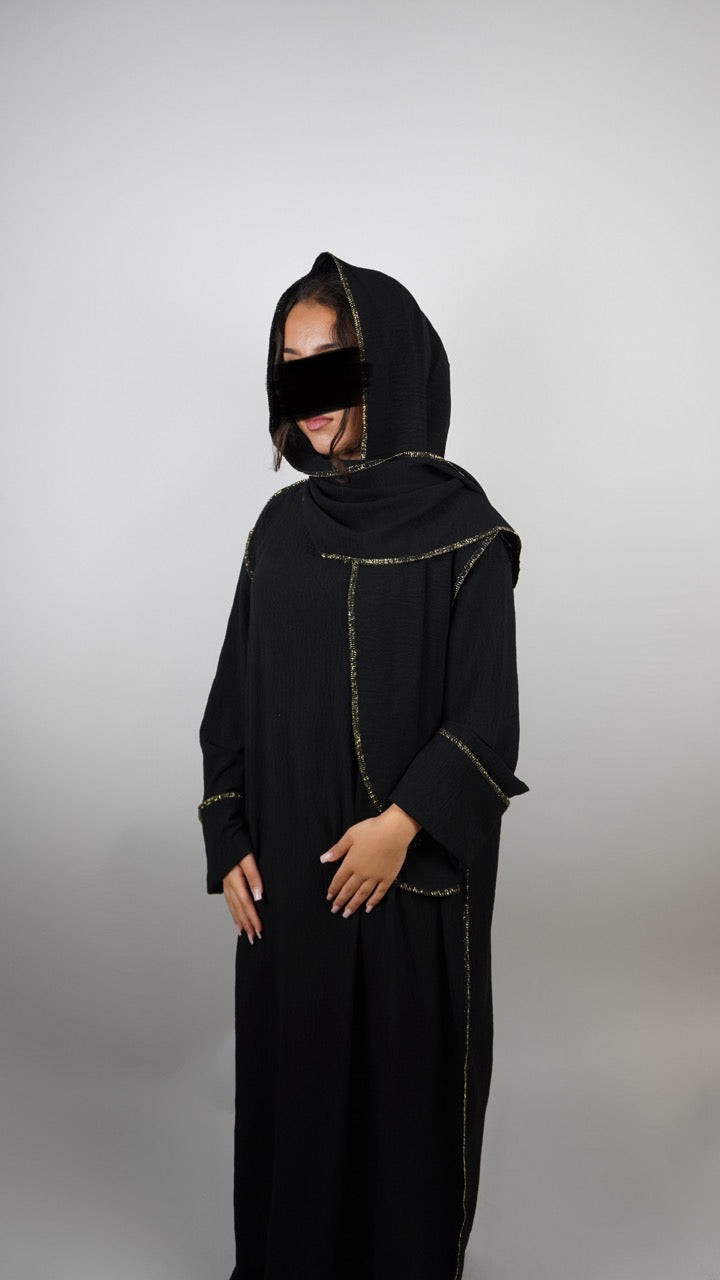 Schwarze Einteiler-Abaya aus strukturiertem Stoff mit integriertem Hijab und goldener Paspel, Dreiviertelansicht.