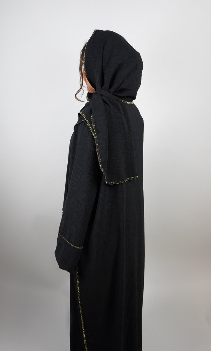 Schwarze Einteiler-Abaya aus Crêpe mit integriertem Hijab und goldener Paspel, gezeigt in Rückansicht.