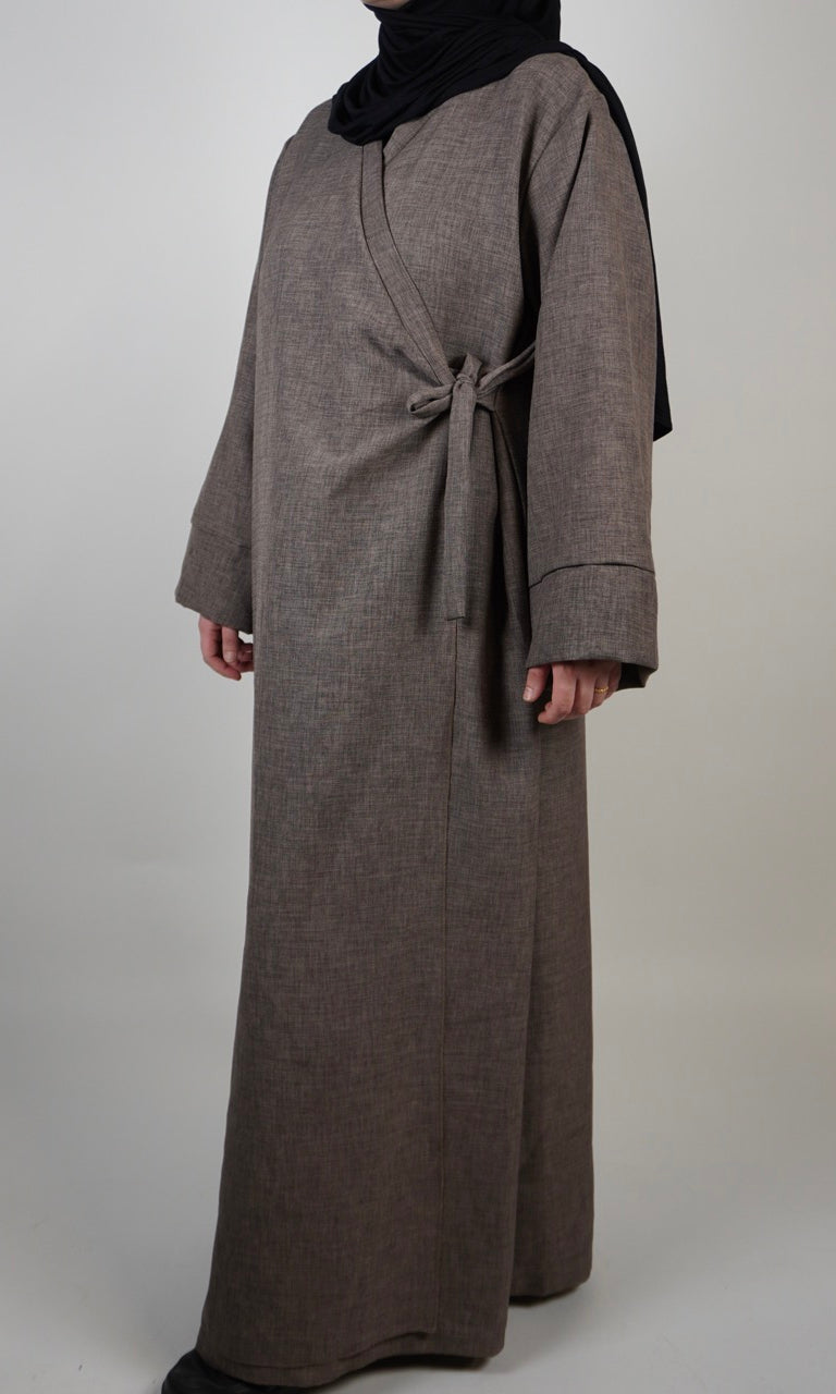 Die Wickelabaya ist in Leinenoptik, beige mit einer kleinen Schleife; sie wird von vorne gezeigt und ist ca. 155 cm lang.