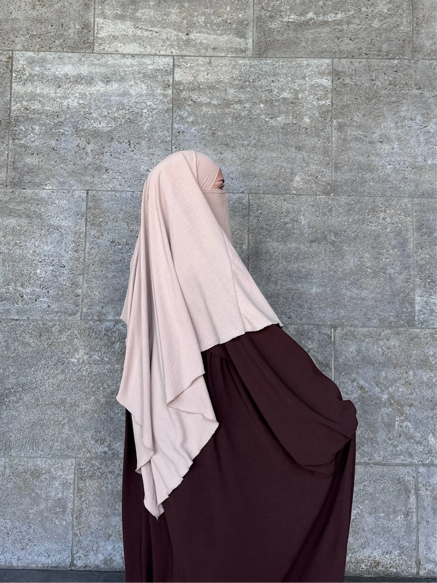 Seitenansicht einer Frau, die eine dunkelbraune Abaya und einen langen, hellbeigen Khimar mit passendem Niqab trägt.