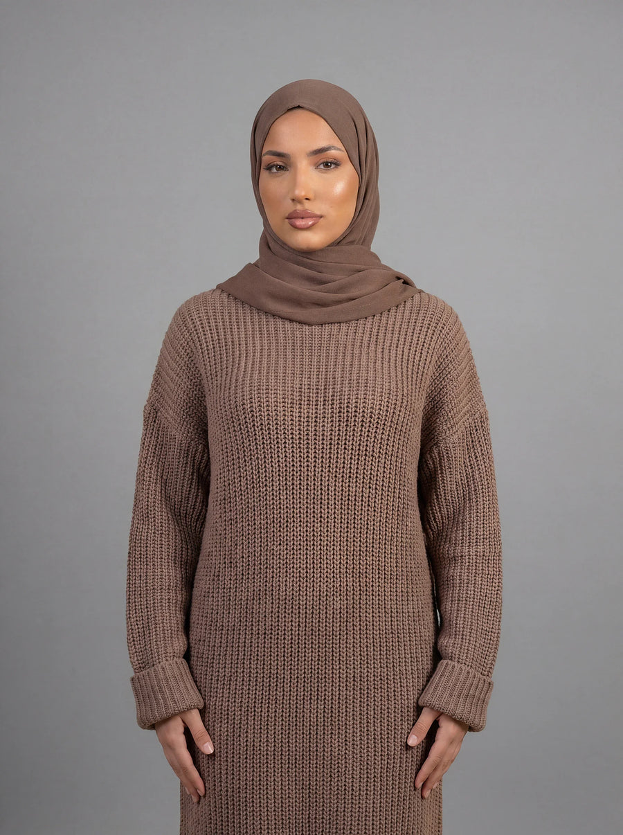 Langes, schwarzes Strickkleid mit einem auffälligen, weißen Wellenmuster an der vorderen Kante und den Ärmeln, getragen von einem Model mit schwarzem Hijab.