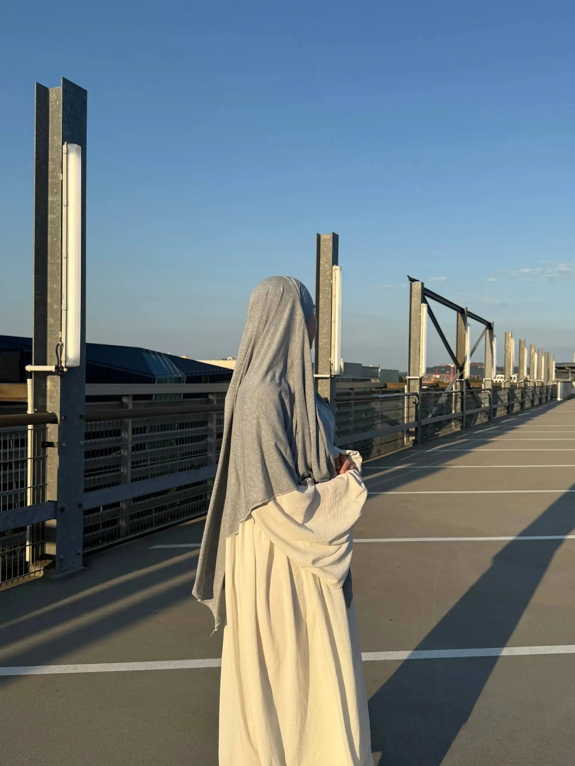 Eine Person trägt einen hellgrauen Jersey-Khimar aus Viskose-Elastan, seitliche Rückenansicht.