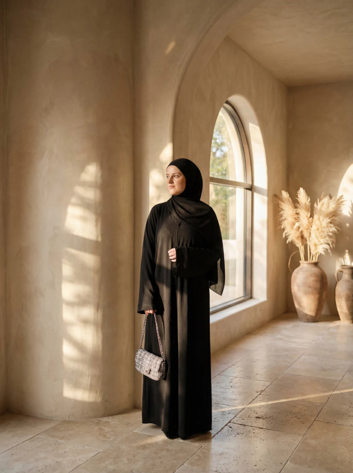 Schwarze Abaya mit gerippter Optik, bodenlang, langen, weiten Ärmeln, oversized, mit silberner Kettentasche, Seitenansicht