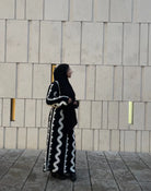 Zu sehen ist ein schwarzes Maxi Strickkleid mit weißen Wellenstreifen und langen Ärmeln, Seitenansicht.