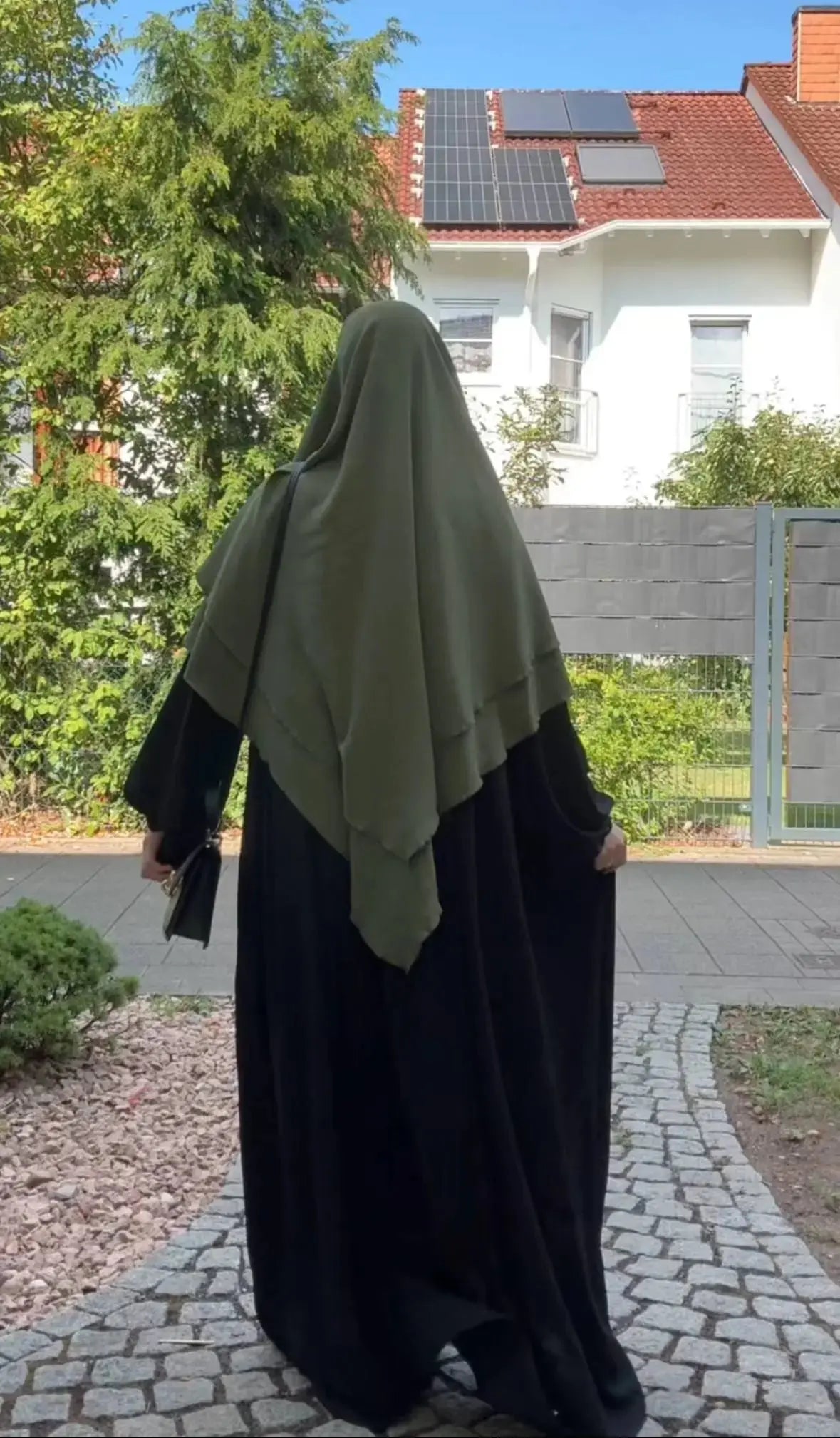 Ein olivgrüner Khimar aus Jazz liegt zweilagig über einer schwarzen Abaya, in Rückansicht.