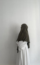 Eine Person trägt einen Jersey Khimar aus Viskose-Elastan in Oliv, seitliche Ganzkörperansicht.