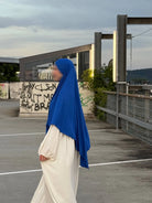Ein Modell trägt einen blauen Jersey‑Khimar aus Viskose‑Elastan (95/5), Seitenansicht.