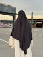 Eine Person trägt einen dunkelgrauen Jersey‑Khimar aus Viskose‑Elastan in Rückenansicht.