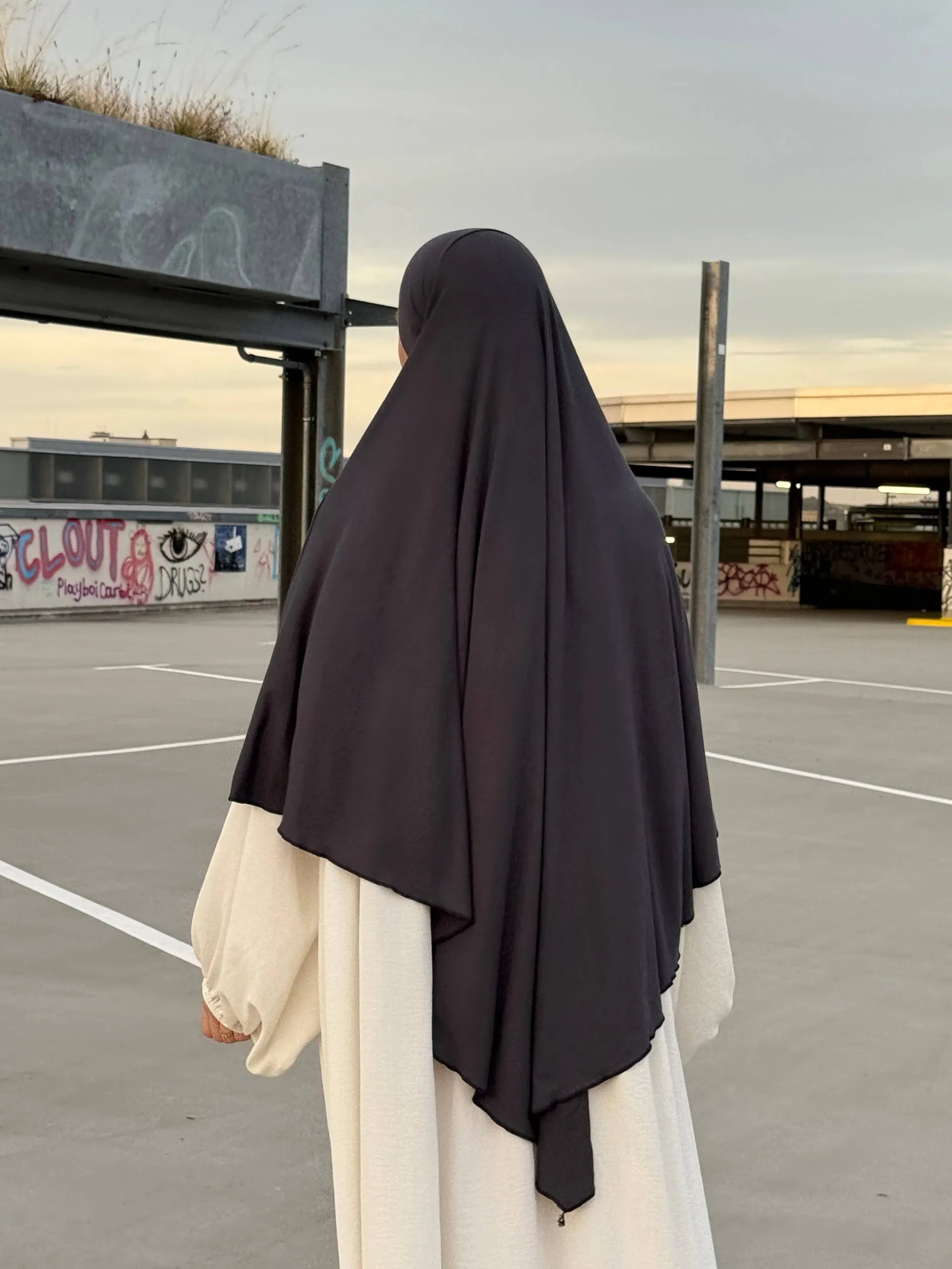 Eine Person trägt einen dunkelgrauen Jersey‑Khimar aus Viskose‑Elastan in Rückenansicht.