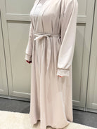 Zu sehen ist eine cremefarbene Open-Abaya aus seidigem Stoff mit Bindegürtel und weiten Ärmeln, Vorderansicht.