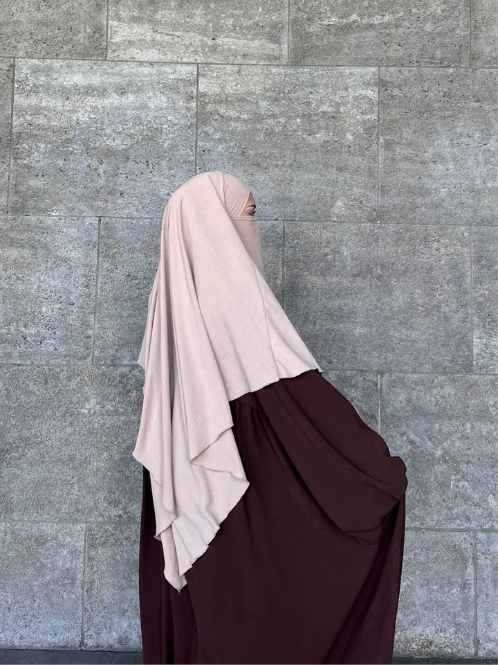 Elegante Frau in einer fließenden, braunen Merve Abaya und einem einlagigen altrosa Khimar von Abayastore.de, die modern und zeitlos wirkt.