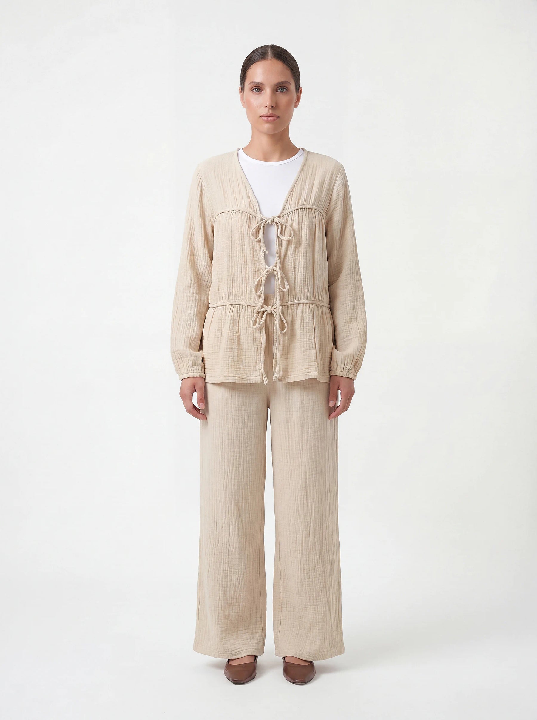 Beige Zweiteiler aus strukturiertem Stoff mit drei Bindeschleifen vorne und weiter Hose, Frontalansicht.