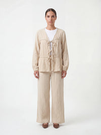 Beige Zweiteiler aus strukturiertem Stoff mit drei Bindeschleifen vorne und weiter Hose, Frontalansicht.
