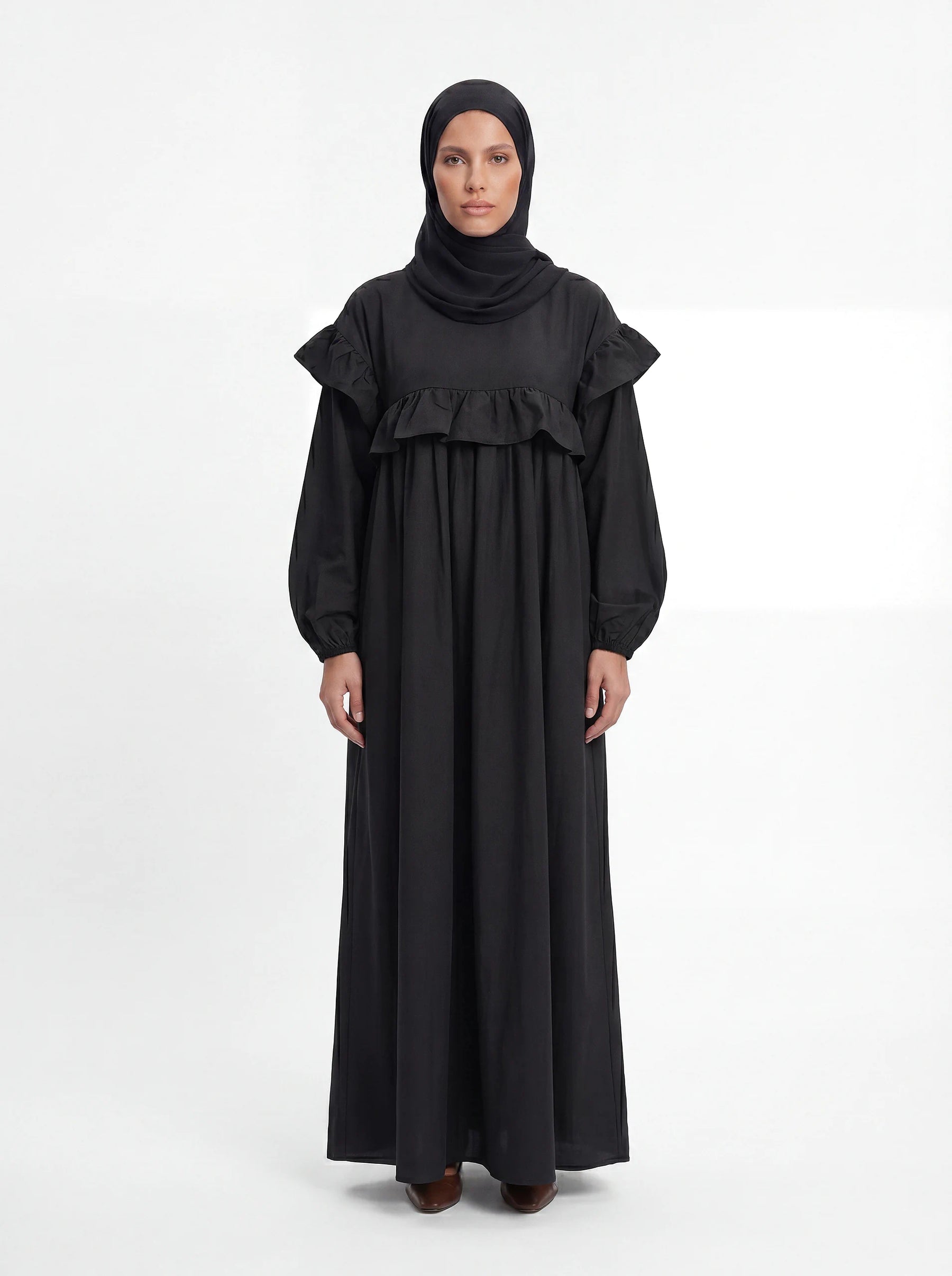 Schwarzes bodenlanges Kleid mit Rüschenbesatz an Brust und Schultern, Frontalansicht.