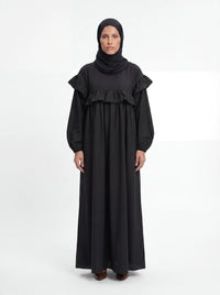 Schwarzes bodenlanges Kleid mit Rüschenbesatz an Brust und Schultern, Frontalansicht.