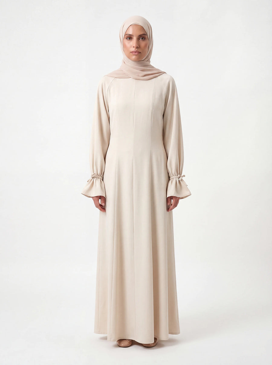 Bodenlanges cremefarbenes Kleid mit gerafften Ärmelabschlüssen und vertikalen Teilungsnähten, Frontalansicht.