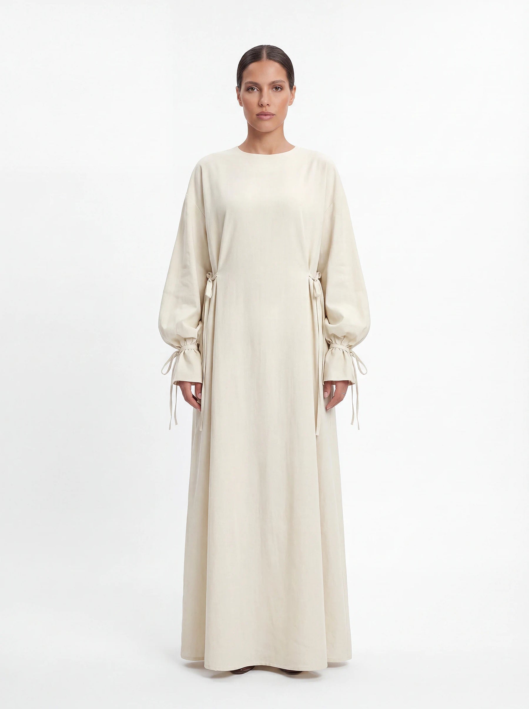 Cremeweiße Abaya mit Schleifendetails an der Taille und den Ärmelabschlüssen, Frontalansicht.
